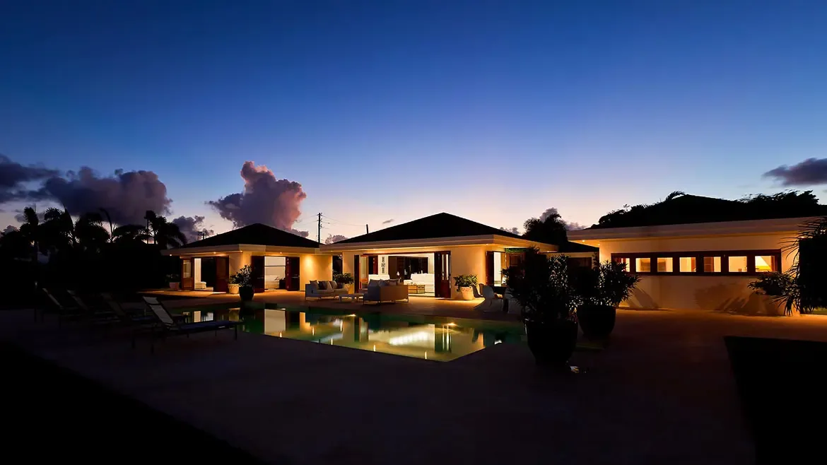 Le Bleu Villa in Anguilla glows beautifully at twilight, with warm architectural lighting reflecting across the private pool and expansive courtyard terrace. This evening exterior highlights the villa's elegant indoor-outdoor design and the refined atmosphere of a premier Caribbean retreat.