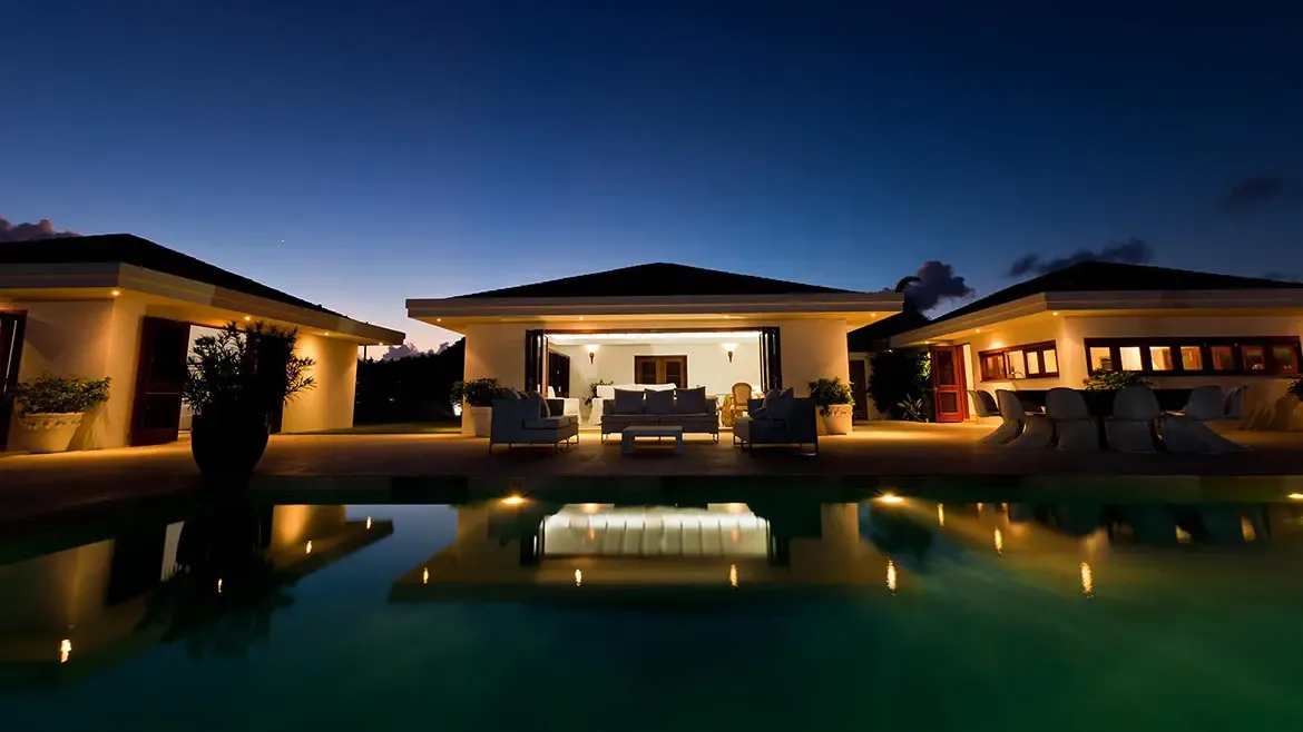 At dusk, Le Bleu Villa presents a serene poolside setting framed by glowing interiors and sophisticated outdoor living spaces. The reflective water and soft evening light create a polished luxury villa image ideal for an Anguilla listing.
