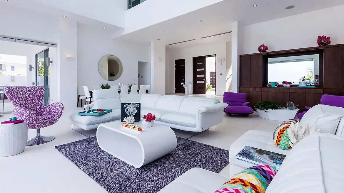 Experience unparalleled luxury in this contemporary Anguilla beach house living area, featuring minimalist white furnishings and elegant purple accents. This sophisticated open-plan space provides the perfect atmosphere for relaxation and high-end entertaining during your Caribbean getaway.
