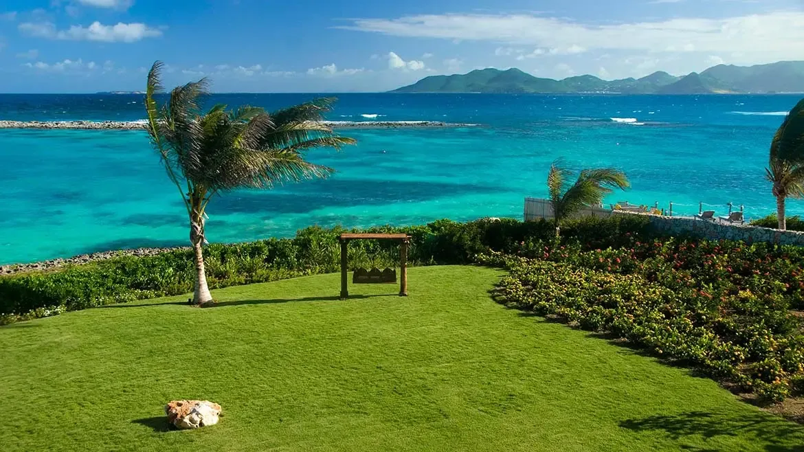 Manicured tropical grounds open to sweeping turquoise sea views, showcasing the exceptional setting of Le Bleu Villa in Anguilla. Palm trees, landscaped lawns, and a dramatic ocean backdrop make this a standout Caribbean estate image.