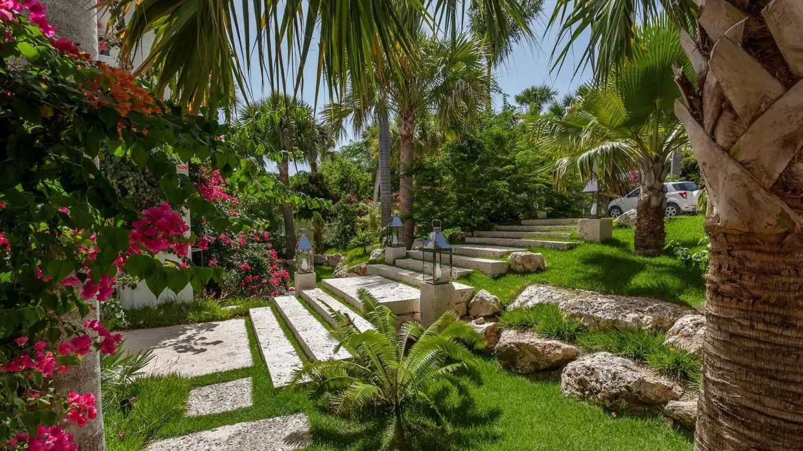 This breathtaking garden entrance at Cerulean Villa features manicured stone pathways and tropical landscaping framed by vibrant bougainvillea and towering palms. Experience the ultimate in Caribbean luxury living with private, serene outdoor spaces designed for tranquility and elegance.