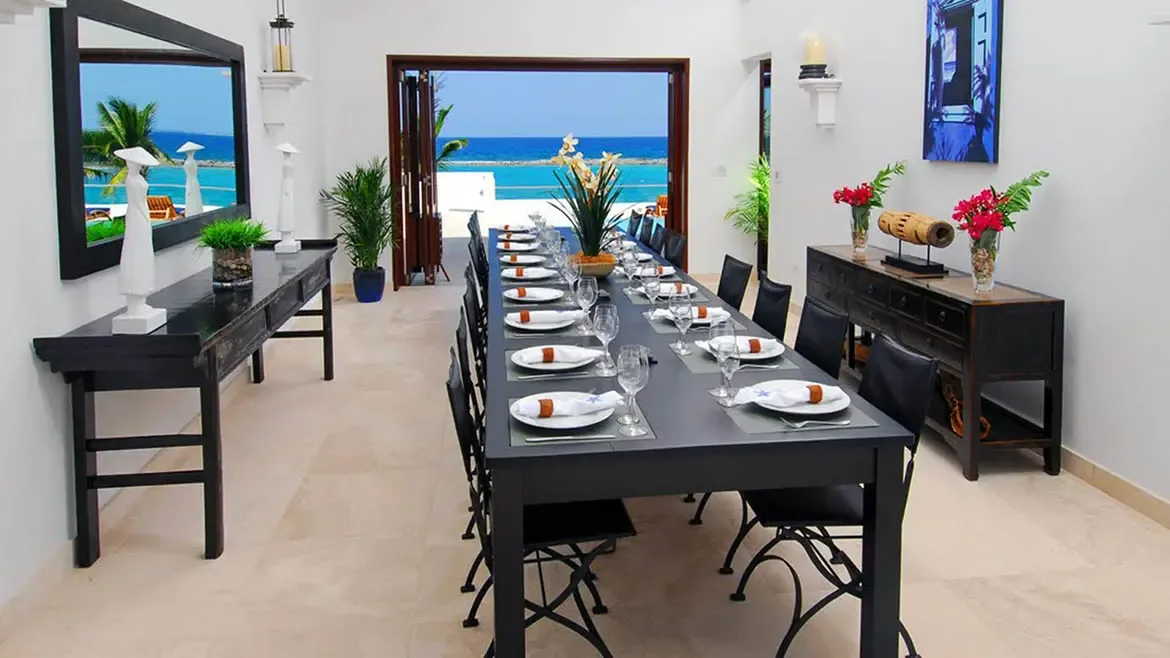 The formal dining room at Le Bleu Villa pairs elegant furnishings with panoramic tropical views for a memorable island dining experience. This interior photo emphasizes both upscale design and the villa's exceptional oceanfront position.