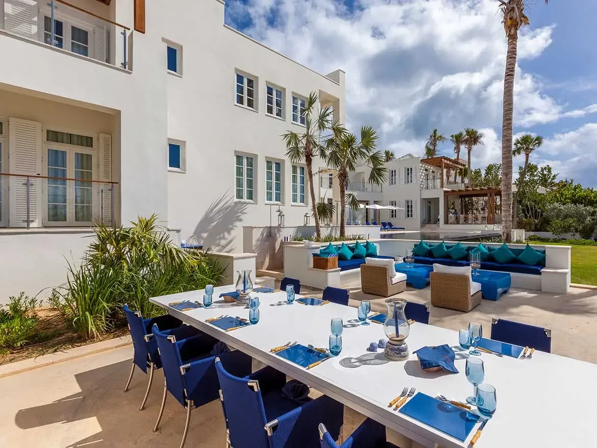 Enjoy elegant al fresco dining on the expansive terrace of Cerulean Villa, featuring a long dining table set against a backdrop of striking white architecture. This luxury beachfront estate in Anguilla offers sophisticated outdoor lounge areas and lush tropical landscaping, perfect for high-end Caribbean entertaining.