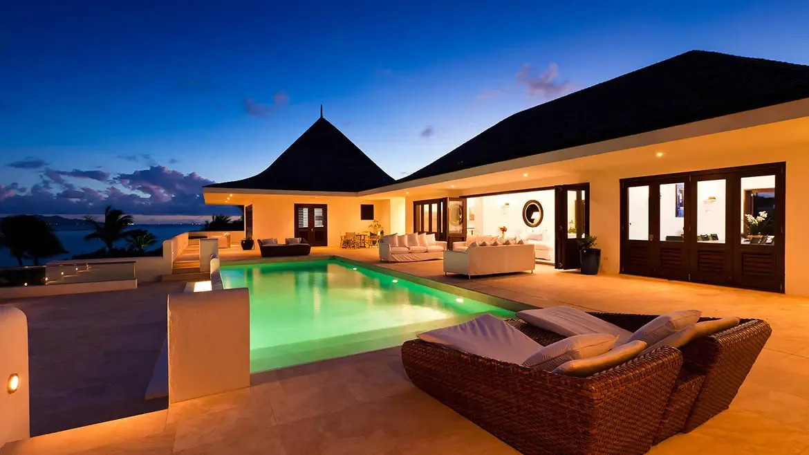 This twilight exterior captures Le Bleu Villa's illuminated pool terrace and inviting outdoor lounge areas against a deep blue evening sky. It is a striking luxury listing image that showcases the property's resort-style ambiance.