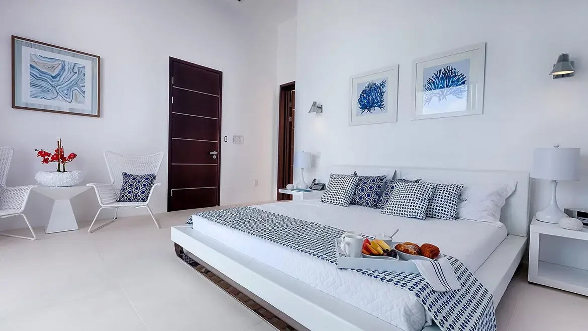 Experience pure coastal elegance in this light-filled bedroom suite at our luxury Anguilla beach house, where minimalist design meets sophisticated Caribbean charm. This serene sanctuary features premium linens and stylish blue-and-white accents, providing the ultimate tranquil retreat for your island getaway.