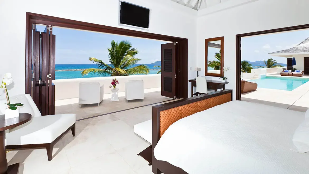 This bright bedroom opens to a private terrace with views of the infinity pool and the Caribbean Sea beyond. The layout reflects Le Bleu Villa's seamless connection between restful interiors and spectacular outdoor scenery.