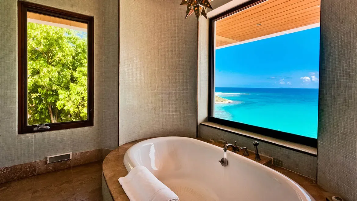 Relax in total serenity within this exquisite ensuite at Zenaida Estate, located at Anguilla's highest elevation. Surrounded by 3 acres of lush tropical gardens, the deep soaking tub provides a front-row seat to sweeping views of the turquoise Caribbean sea, blending indoor luxury with the island's natural beauty.