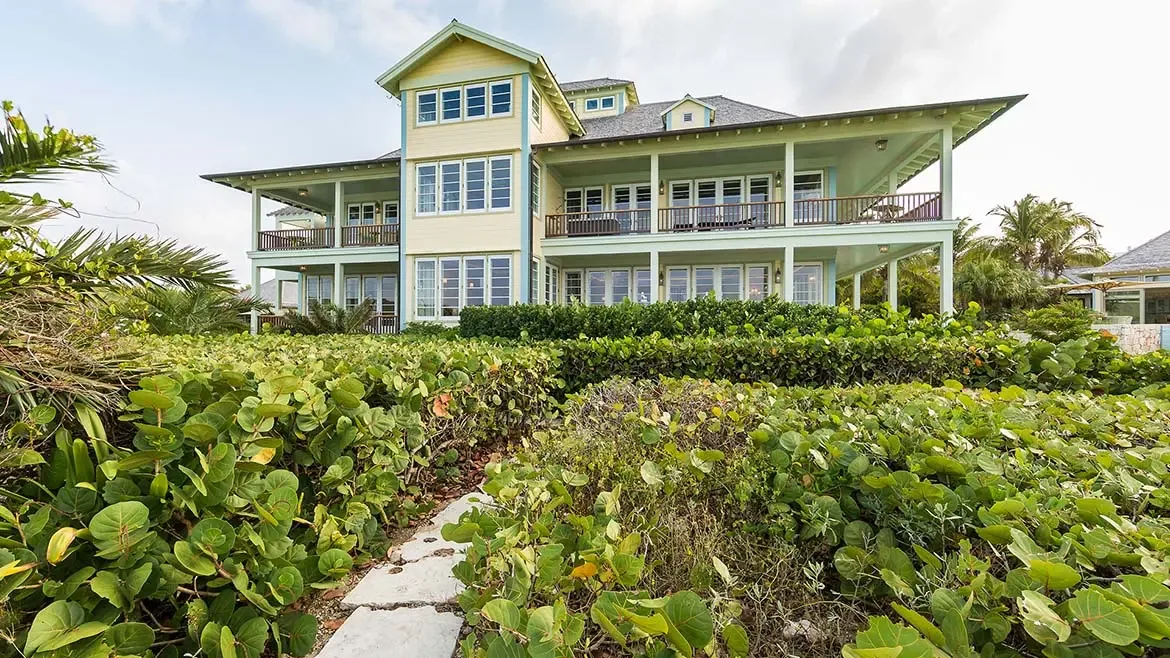 An aerial perspective of Villa Santosha reveals professional tennis courts nestled amidst lush tropical gardens, perfectly positioned to capture breathtaking views of the sparkling Caribbean Sea at Long Bay.