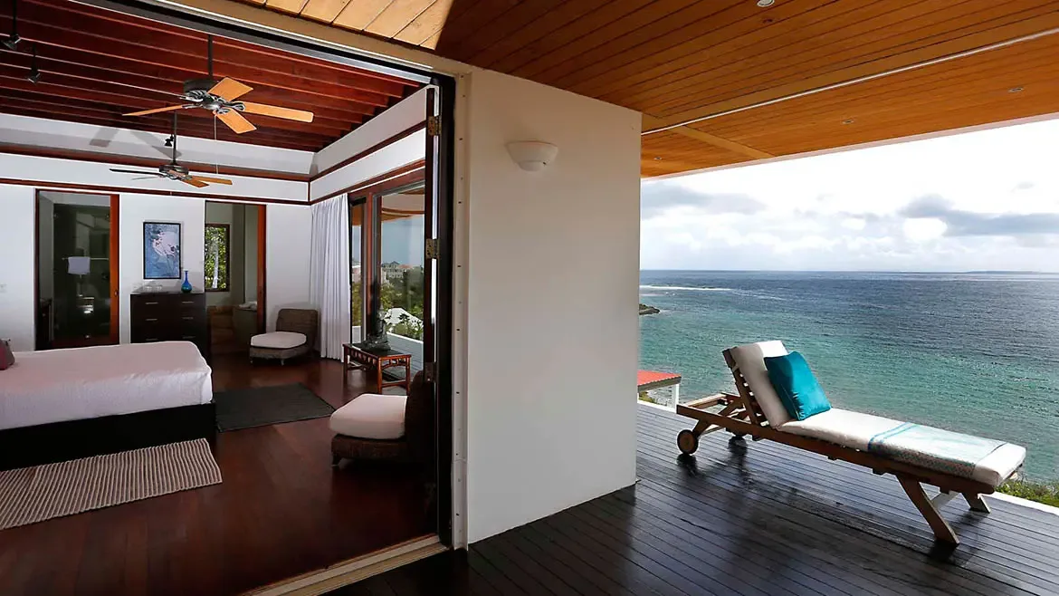 Perched at Anguilla's highest elevation, the master suite at Zenaida Estate offers a seamless transition from its refined interior to a private deck with sweeping views over three acres of lush gardens and the turquoise sea.