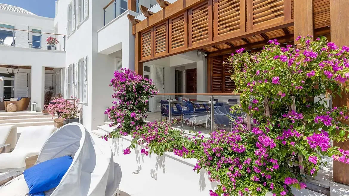 Experience unparalleled outdoor living at Cerulean Villa in Anguilla, featuring a stunning terrace draped in vibrant pink bougainvillea and elegant wooden accents. This luxury Caribbean rental offers a sophisticated alfresco dining area and serene lounging spaces, perfect for enjoying the island's tropical beauty in complete privacy.
