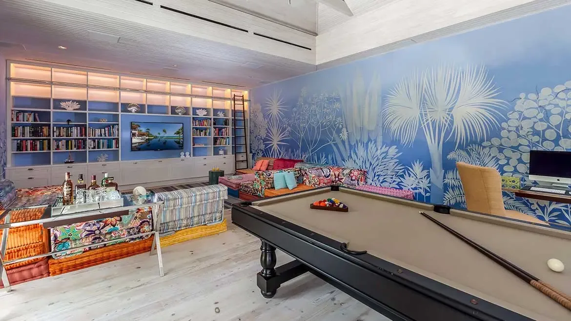 Relax and entertain in the vibrant game room of Cerulean Villa, featuring a professional pool table and plush, colorful modular seating. This expansive entertainment space includes a custom media wall, private bar area, and stunning tropical murals, perfect for unforgettable nights during your luxury Anguilla getaway.