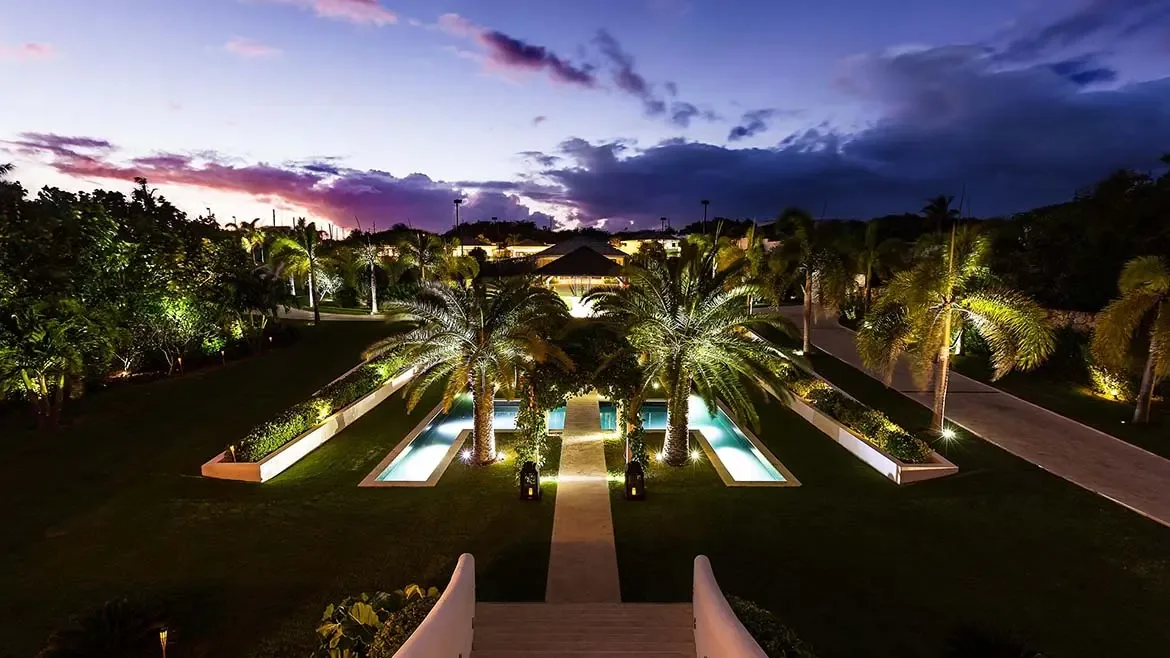 At dusk, Le Bleu Villa's formal garden and reflecting pools are beautifully lit, creating a dramatic resort-style arrival sequence. This exterior image adds a strong sense of scale, symmetry, and evening elegance to the listing.