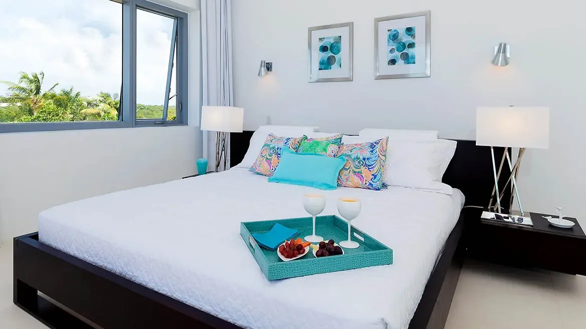 Wake up to tropical paradise in this modern Anguilla beach house master suite featuring crisp white linens and vibrant Caribbean accents. Enjoy a private breakfast in bed while taking in lush island views through expansive windows in this elegantly appointed luxury villa rental.
