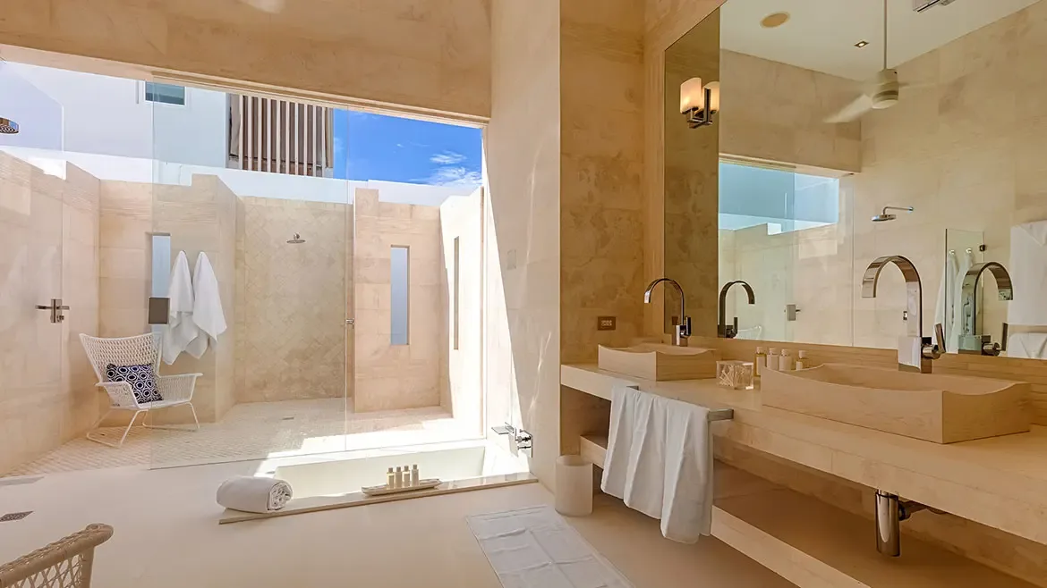 Experience ultimate relaxation in this spa-inspired master bathroom, featuring a deep sunken bathtub and dual vessel sinks. The space flows effortlessly into a private, sun-drenched outdoor shower area, perfectly capturing the essence of indoor-outdoor luxury living in Anguilla.
