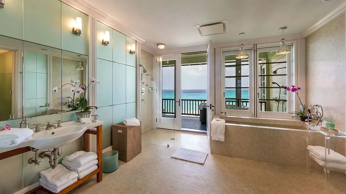 Relax in the thoughtfully designed family room at Villa Santosha, where rustic charm meets coastal elegance. Featuring vaulted sky-blue ceilings and a built-in window seat, this cozy retreat offers breathtaking views of the turquoise Caribbean Sea across Long Bay.