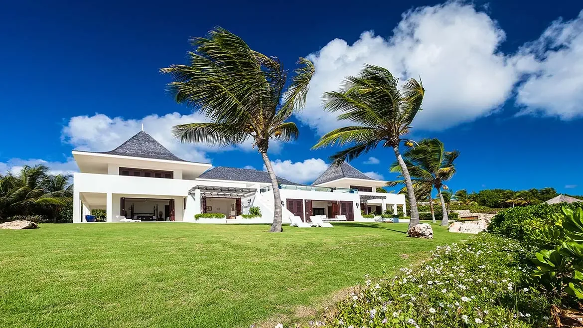 Le Bleu Villa's white façades, manicured lawn, and tropical planting create a crisp and welcoming estate presentation under bright Caribbean light. This image reinforces the property's polished landscaping and private villa character.