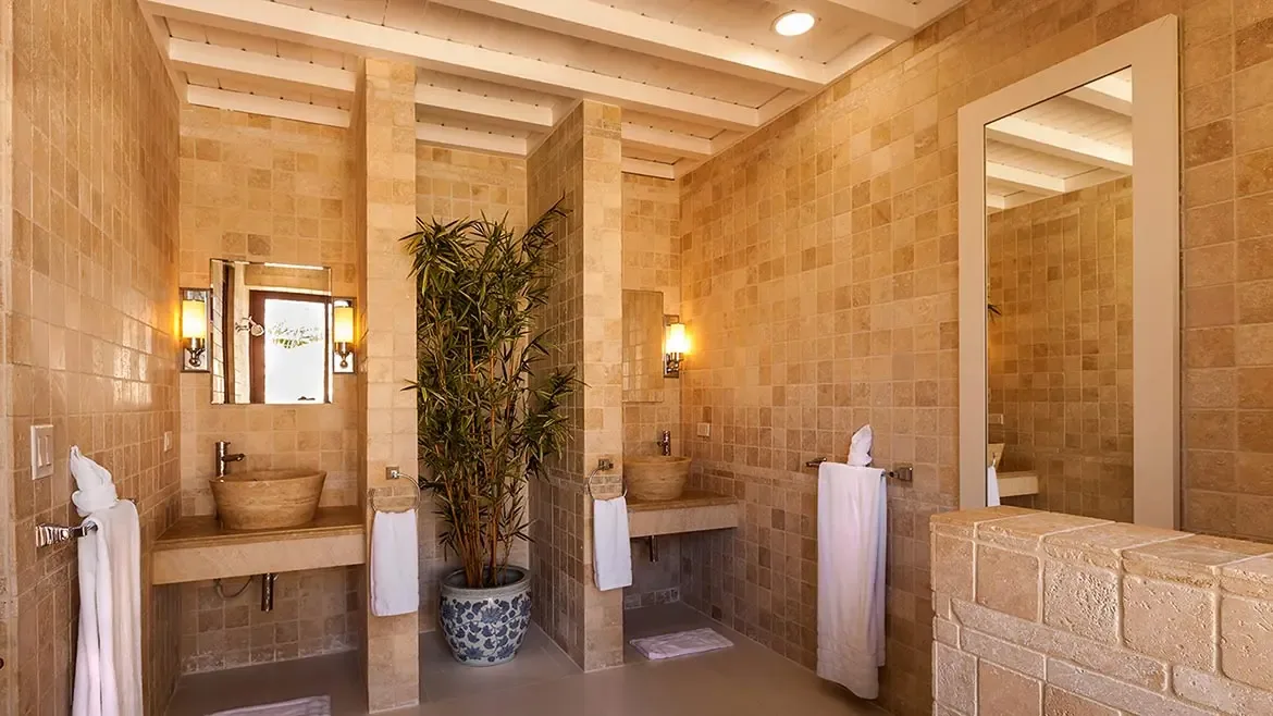 Indulge in a tranquil spa experience within this masterfully crafted bathroom at Villa Indigo, featuring warm natural stone finishes and elegant vessel sinks. This serene oasis perfectly captures the essence of luxury Caribbean living, offering a private retreat for rejuvenation during your stay in Anguilla.