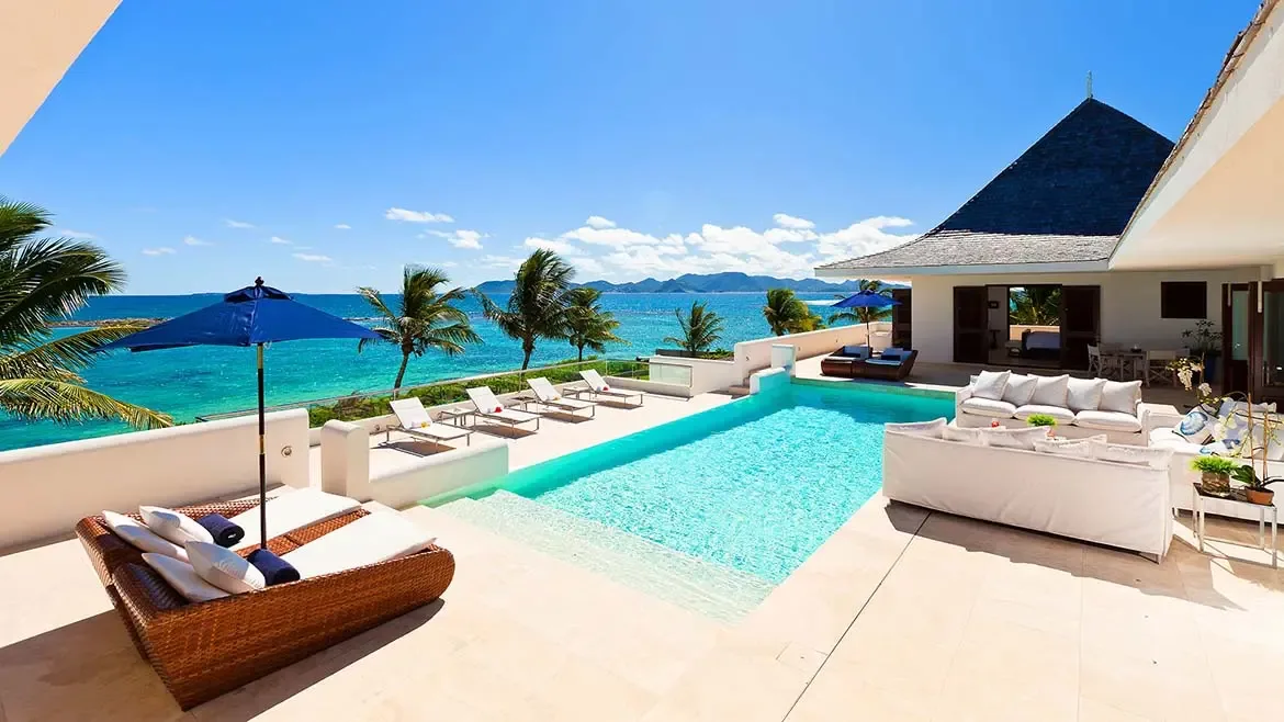 Poolside seating, blue umbrellas, and uninterrupted sea views give this exterior image a classic luxury Caribbean resort feel. It presents Le Bleu Villa as an exceptional oceanfront escape with well-designed outdoor gathering spaces.