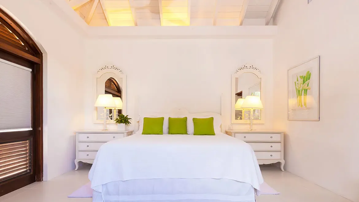 Experience serene luxury in this elegantly designed bedroom at Villa Indigo, featuring high vaulted ceilings and a crisp white color palette accented by vibrant green touches. This tranquil space in our premier Anguilla villa rental offers the perfect sanctuary for rest and rejuvenation during your Caribbean escape.
