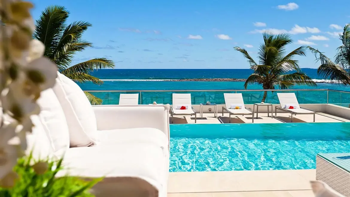 Framed by palms and designer lounge seating, Le Bleu Villa's infinity pool overlooks vivid turquoise water in one of the property's most marketable scenes. The bright tropical light adds clarity and energy to this high-impact listing image.