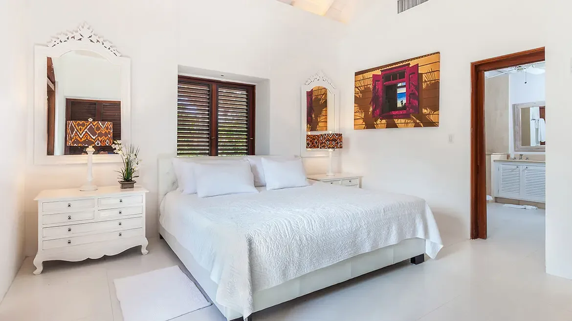 Experience the ultimate in tropical luxury within this bright and airy bedroom suite at Villa Indigo in Anguilla. The elegant white-on-white decor is accented by vibrant local art and offers seamless access to a private, modern ensuite bathroom.