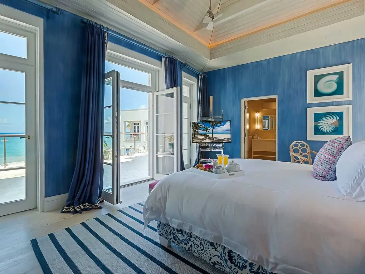 Wake up to breathtaking Caribbean views in this stunning oceanfront master suite at the luxury Cerulean Villa in Anguilla. The bedroom's vibrant blue palette and elegant coastal decor create a serene sanctuary, complete with private terrace access for a truly immersive island experience.