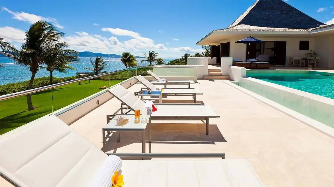 A wide-angle view of the stone patio and infinity pool highlights the scale of Le Bleu Villa's oceanfront outdoor areas. Clean lines, lounge seating, and bright Caribbean light make this a strong hero image for the listing.