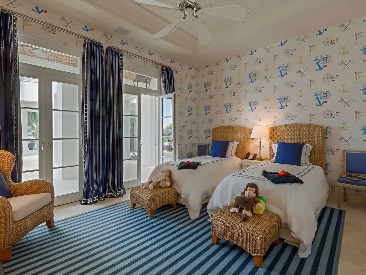 This charming nautical-themed guest suite at Cerulean Villa features twin beds with wicker headboards and playful marine-inspired wallpaper. Bright blue striped accents and natural textures create an inviting and luxurious retreat for children or additional guests.