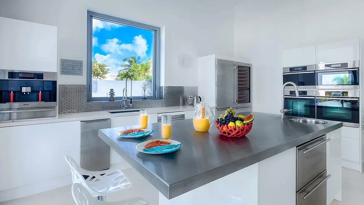 This state-of-the-art gourmet kitchen in our luxury Anguilla beach house features sleek stainless steel finishes and professional-grade appliances for the ultimate culinary experience. Enjoy a sun-drenched breakfast at the expansive island while gazing through large windows at the lush tropical landscape and vibrant Caribbean sky.
