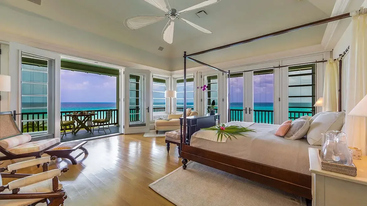 Experience unparalleled luxury in the master suite of Villa Santosha, where a classic four-poster bed and private terrace offer breathtaking Caribbean views of Long Bay's azure waters.
