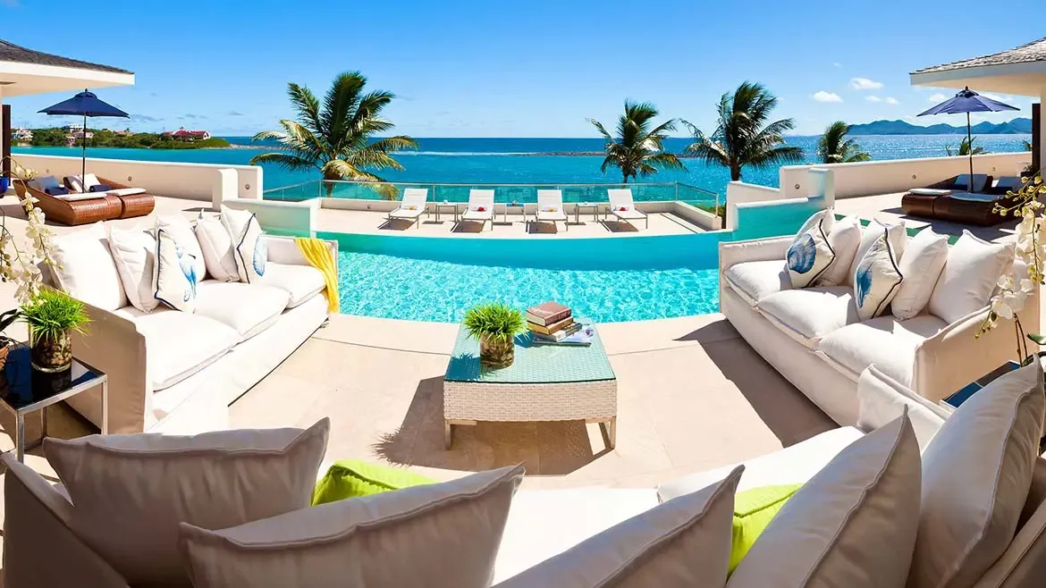 Le Bleu Villa's infinity pool extends toward the horizon, pairing white outdoor furnishings with expansive Caribbean sea views. The result is a clean, aspirational image that performs well for luxury villa marketing.