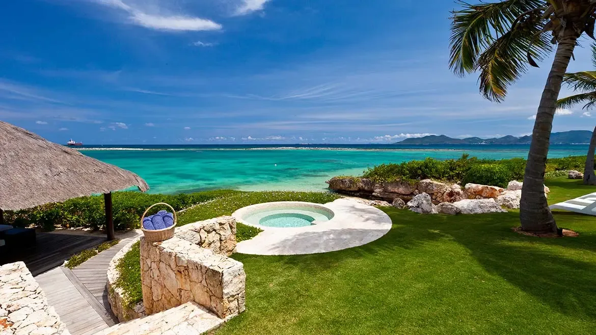 A high-angle view of the lawn, circular plunge pool, and thatched gazebo showcases another private outdoor retreat within the estate. With vivid water and mature palms in the background, the image strengthens the property's resort-style appeal.