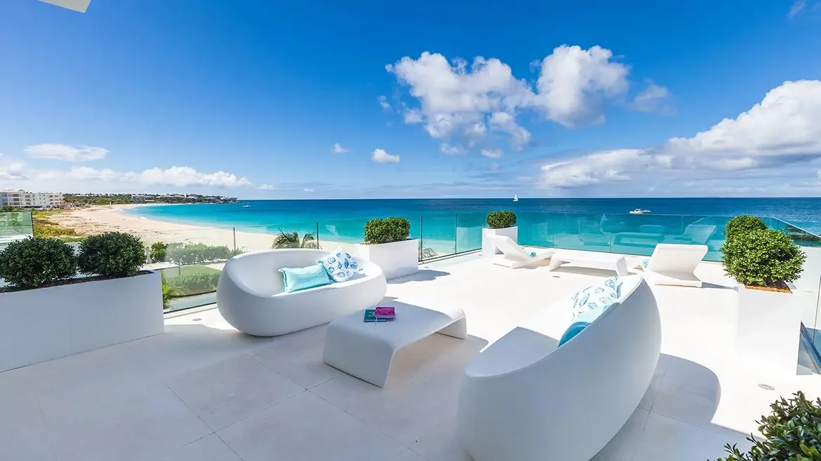 Experience ultimate Caribbean luxury on this expansive rooftop terrace overlooking the pristine turquoise waters of Anguilla. This stunning outdoor living space features contemporary white furniture and sleek glass railings, offering unobstructed panoramic views of the sandy beach and ocean beyond.