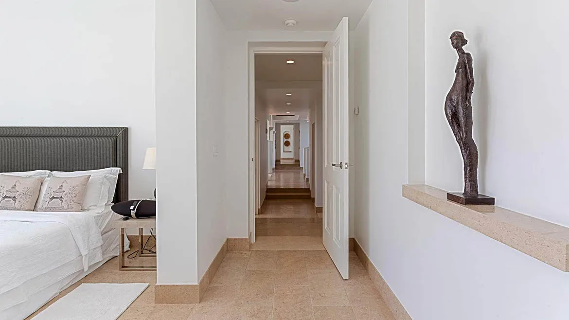 A glimpse into a serene white bedroom and hallway featuring minimalist art and neutral stone flooring.
