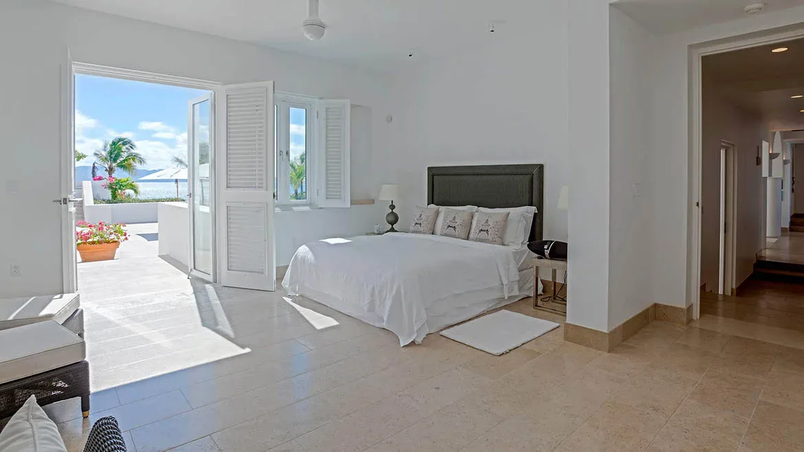 Serene white bedroom with stone flooring and open-concept access to the outdoor patio.