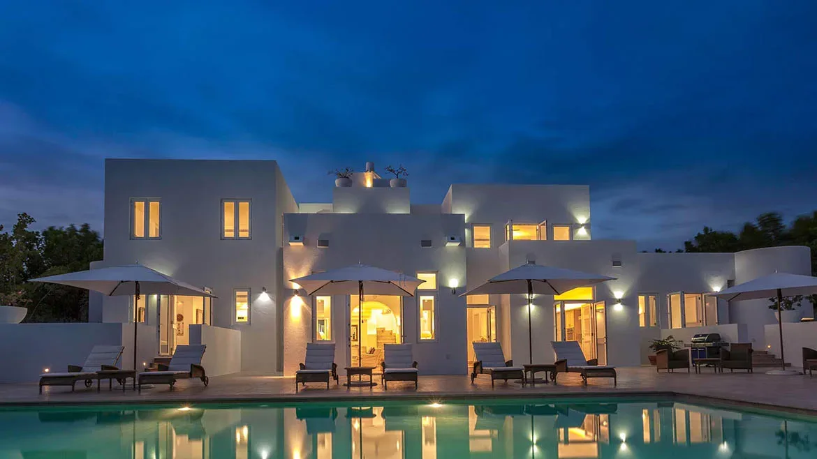 Exterior view of the white modern Villa Arushi at twilight with illuminated interiors and a reflecting swimming pool.