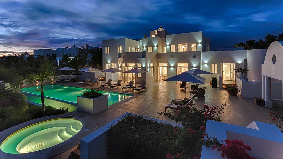 Twilight view of Villa Arushi featuring an illuminated swimming pool, hot tub, and white architecture.