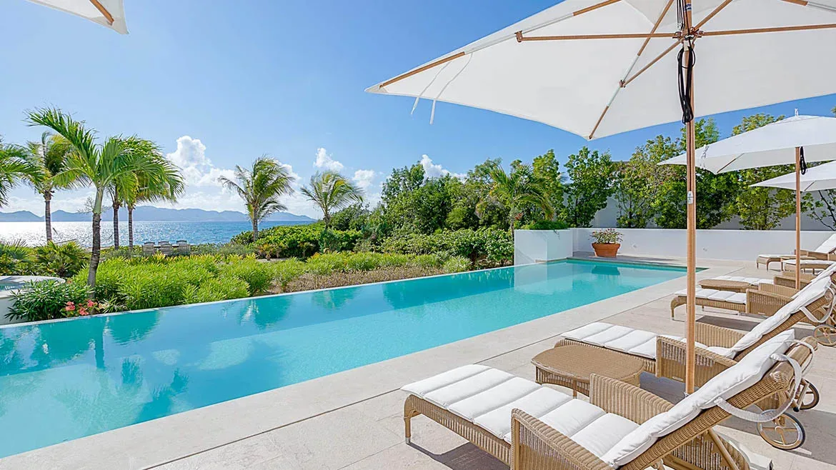 Long swimming pool and sunbathing area at Villa Arushi surrounded by lush tropical greenery and white umbrellas.