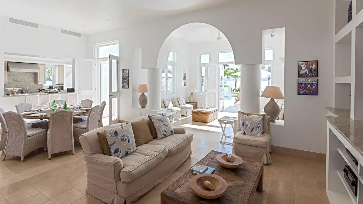 Open concept living and dining area in Villa Arushi featuring white walls, beige furnishings, and arched doorways.