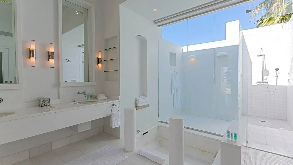 Modern white bathroom at Villa Arushi featuring a glass-enclosed shower and double vanity.