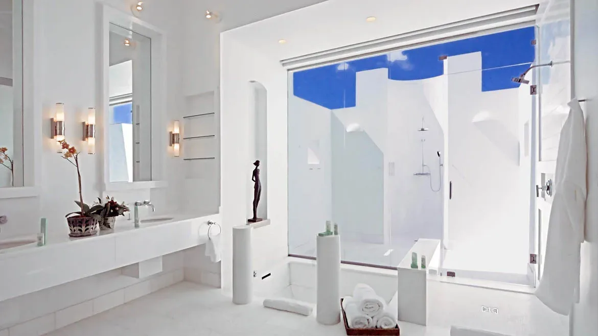 A bright, all-white modern bathroom featuring a double vanity, minimalist decor, and a glass-enclosed shower.