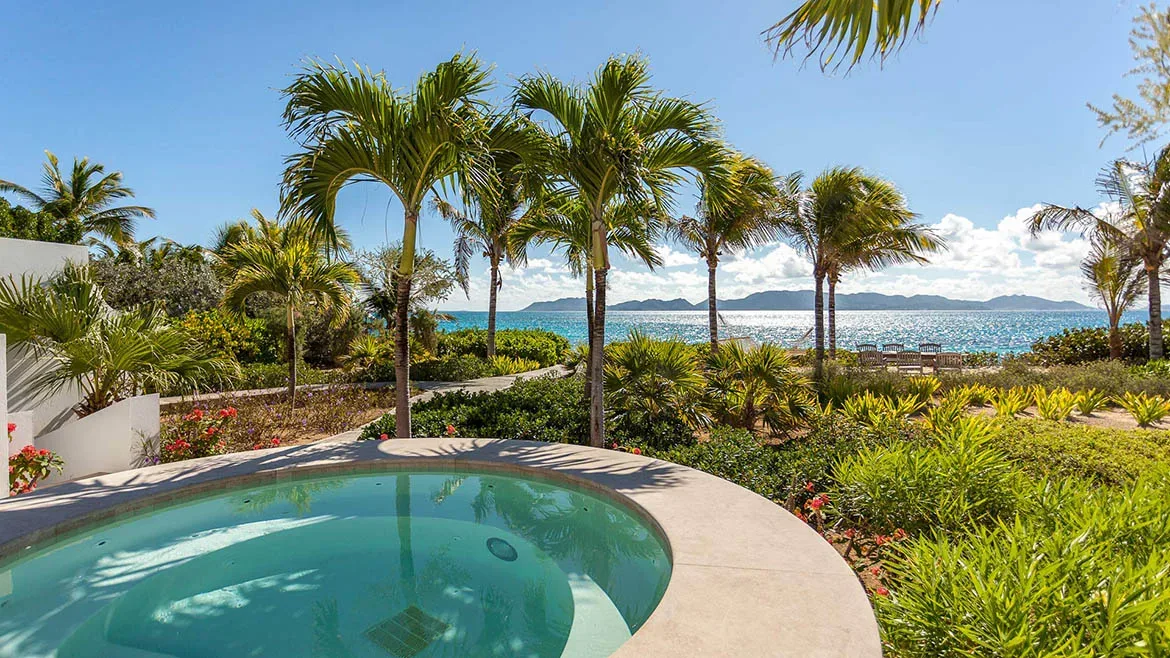 Circular plunge pool surrounded by lush tropical gardens and palm trees with a view of the distant islands.