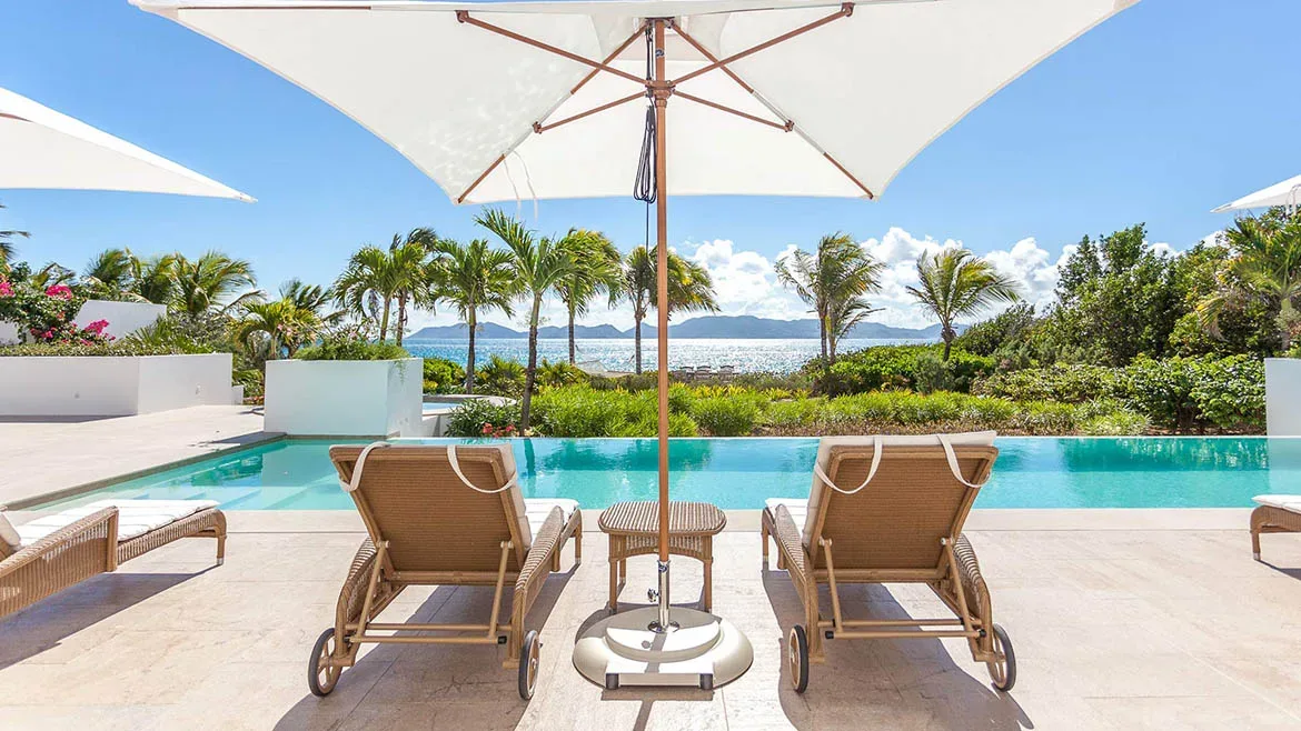 Luxury pool deck at Villa Arushi with white parasols, lounge chairs, and a view of the ocean horizon.