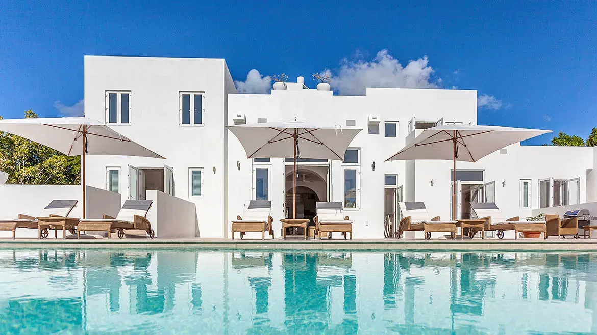 Low angle shot of the swimming pool reflecting the facade of the white luxury villa.