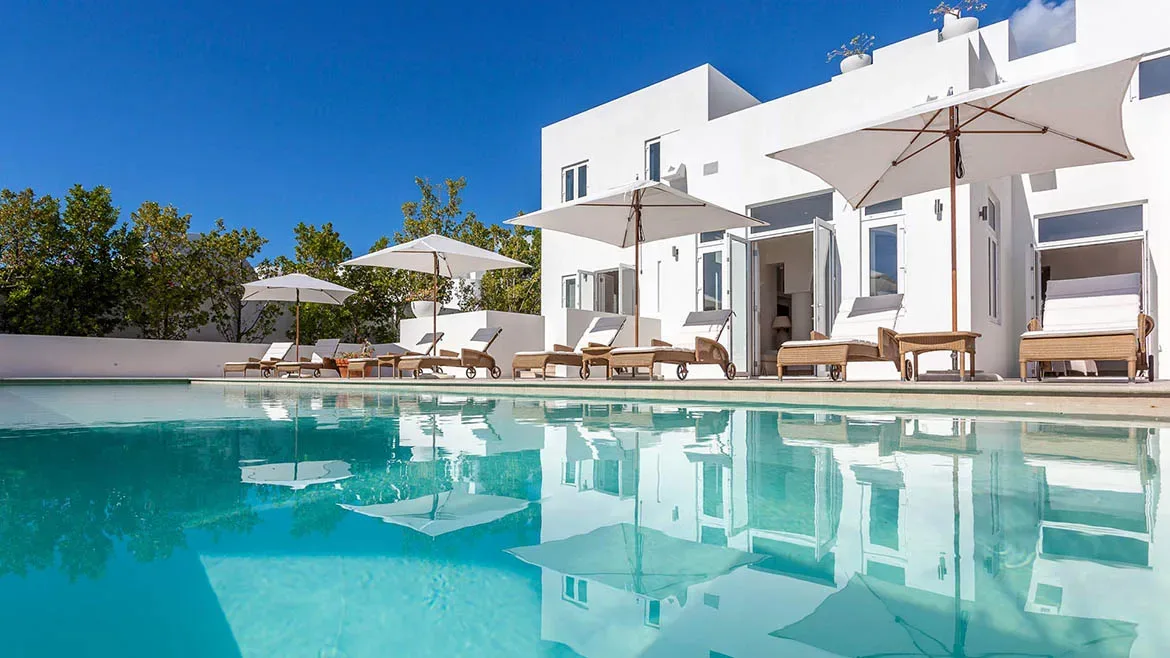 Crystal clear swimming pool reflecting the white villa walls and white patio umbrellas.