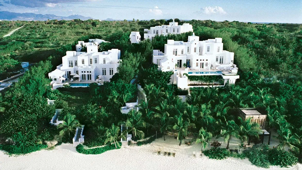 Aerial view of the white Elements villa complex nestled among dense tropical greenery and palms on a white sand beach.
