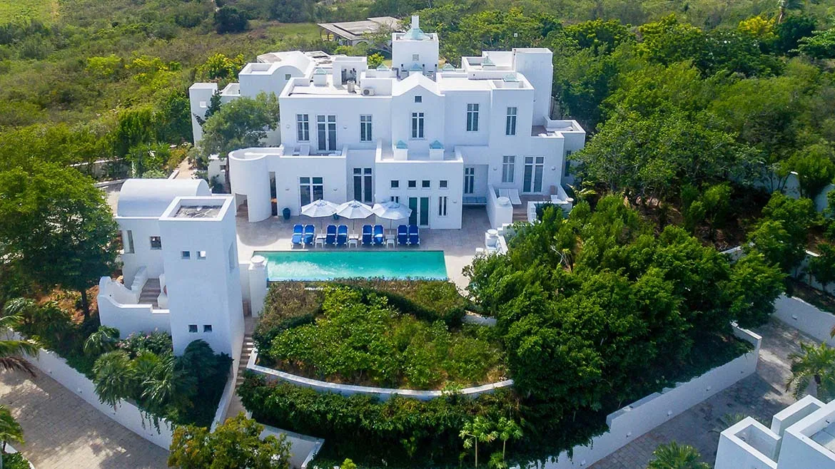 Aerial view of the white luxury villa with a swimming pool and lush green gardens in Long Bay, Anguilla.