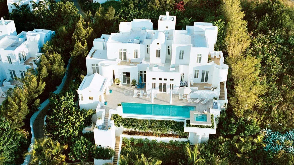 High-angle shot of a white luxury villa with a sparkling turquoise swimming pool and manicured gardens.