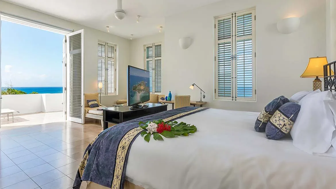 Airy bedroom suite with a king-size bed, white linens, and open-concept access to a balcony.