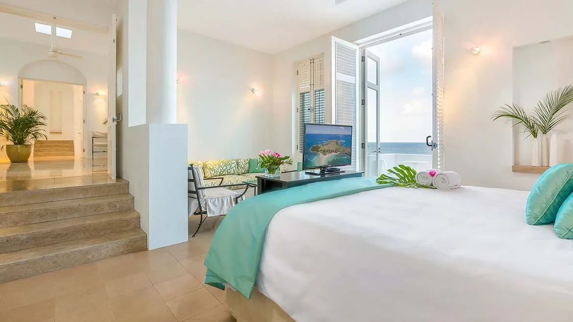 Modern bedroom with a white bed and teal accents, looking out toward the Caribbean Sea.